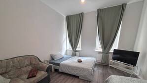 A bedroom with a bed, a sofa, a TV, and a window with curtains.