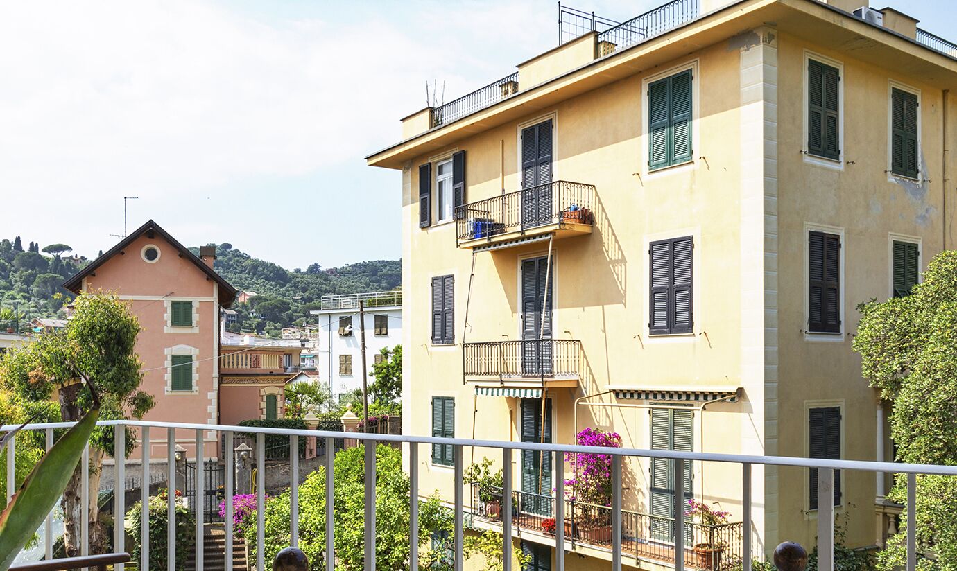 A multi-story building with balconies, a staircase, and surrounding greenery.