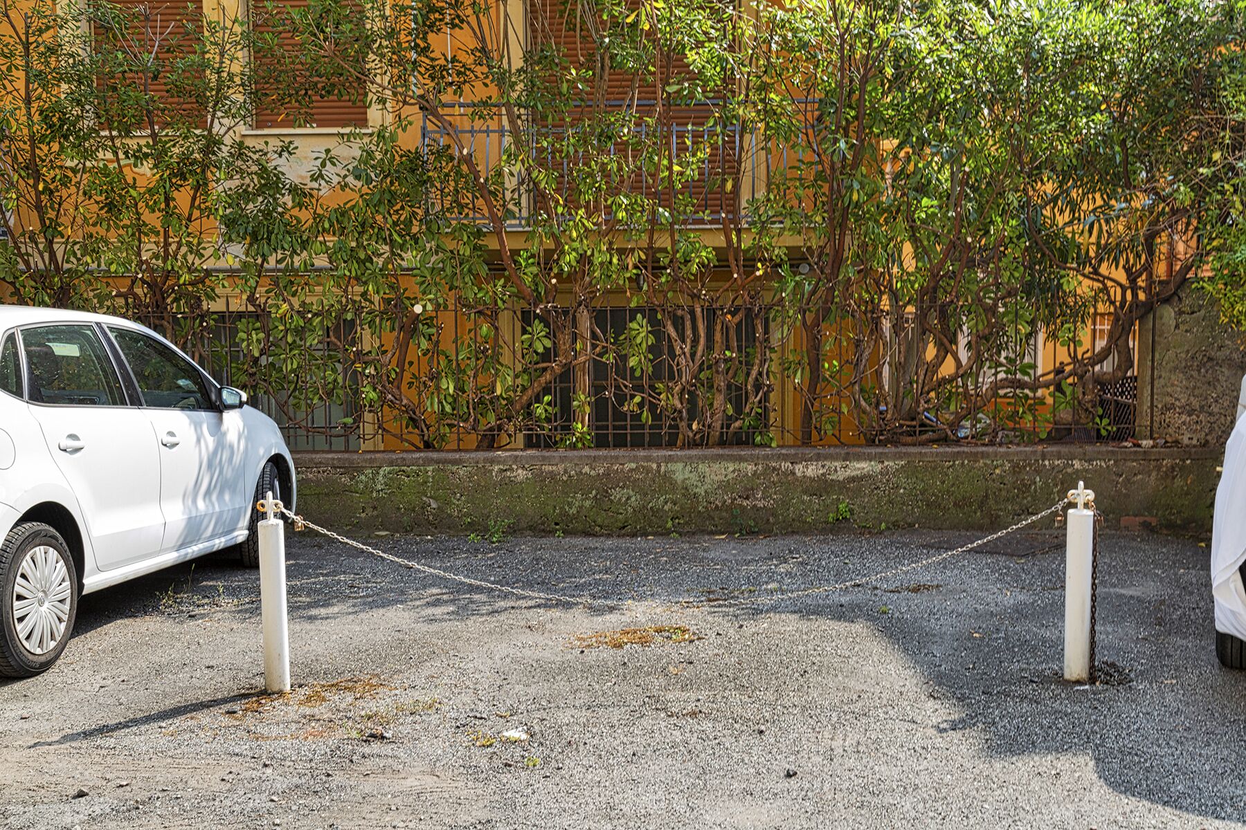 Un coche blanco estacionado frente a un edificio con una barrera de cadena.