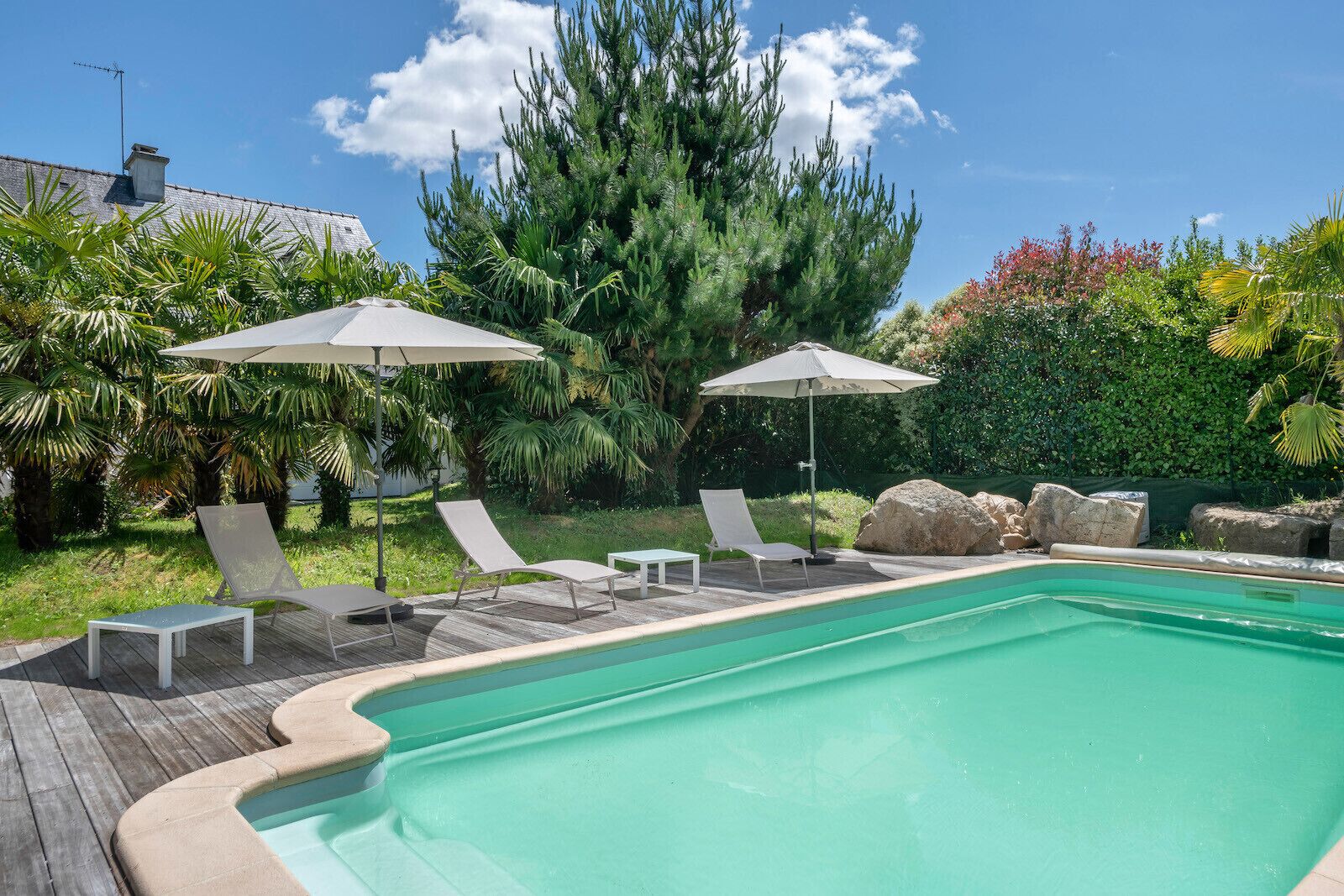 Ein Pool mit Liegestühlen und Sonnenschirmen, umgeben von viel Grün und Felsen.