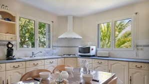 A kitchen with white cabinets, a stove, a microwave, and a toaster. There are windows with a view of palm trees. - Superb house for 8 in Crach with swimming pool (Crach)