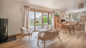 A spacious living area with a large sliding glass door leading to a garden, wicker furniture, a kitchen with wooden cabinets, and a dining table. - Bright house with large terrace in La Roche-Bernard (La Roche-Bernard)