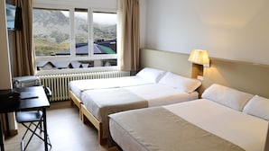 Habitación de hotel con dos camas, un escritorio, una lámpara y una ventana con vista a las montañas.