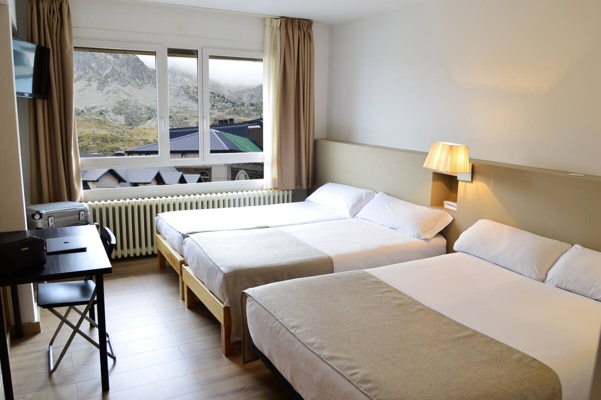 Een hotelkamer met twee bedden, een bureau, een lamp en een raam met uitzicht op bergen.