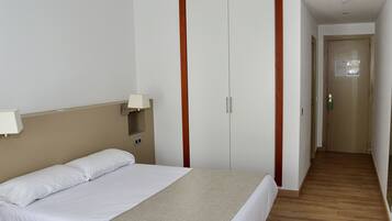 Una camera d'albergo con un letto, un armadio, un comodino e una lampada.