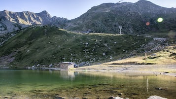Eine bergige Landschaft mit einem klaren See, einem kleinen Gebäude und einer Straße.