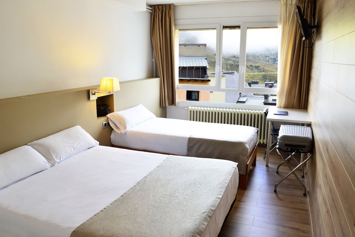 Een hotelkamer met twee bedden, een bureau, een stoel en uitzicht op een bergachtig landschap.