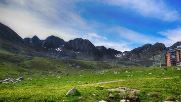 A mountainous landscape with a clear sky, a grassy field, and a building with multiple floors.