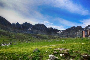A mountainous landscape with a clear sky, a grassy field, and a building with multiple floors.