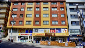 Un hotel de varios pisos con fachada amarilla y marrón, que cuenta con un restaurante en la planta baja y un hidrante visible.