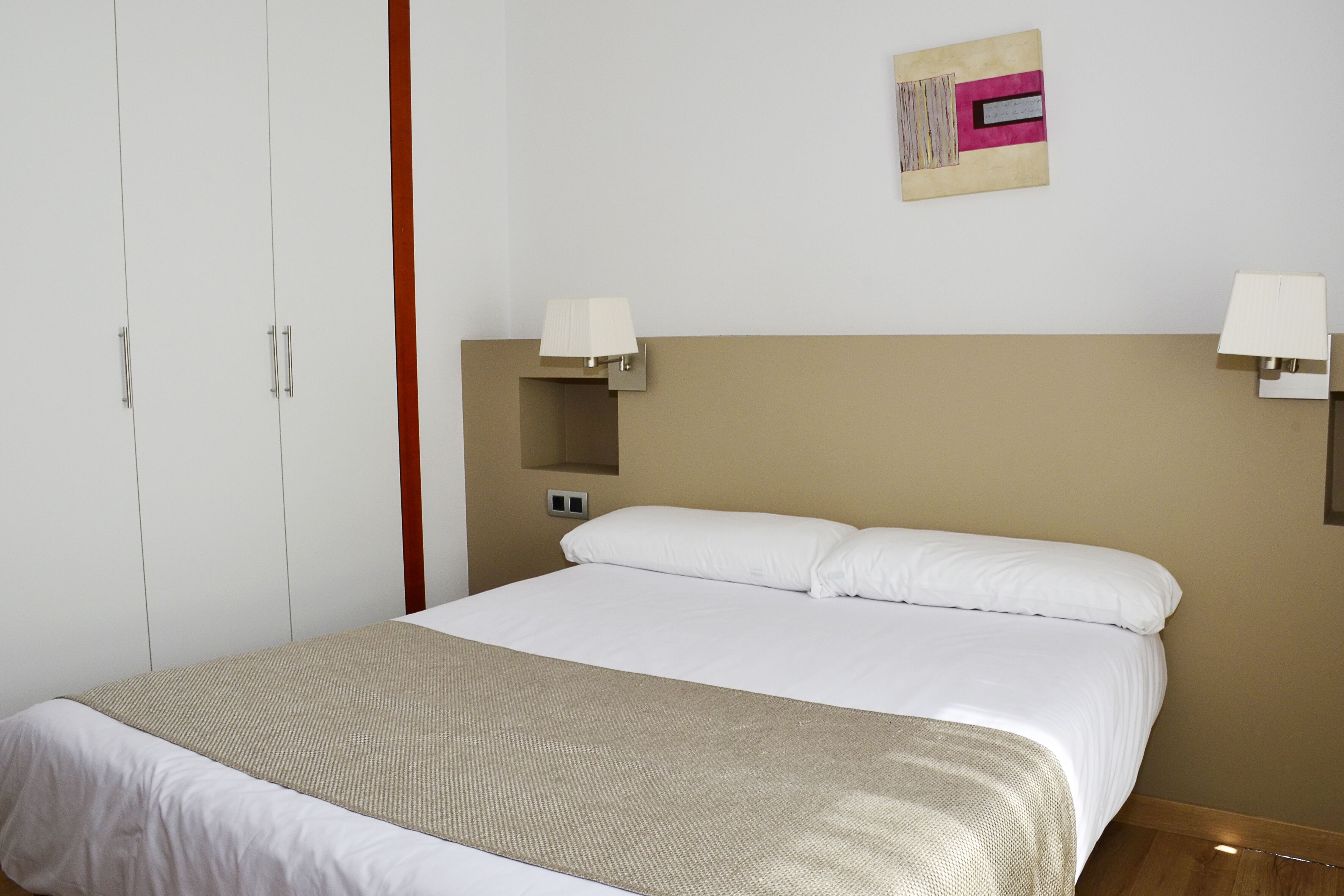 A neatly made bed with white linens, a beige throw blanket, and two bedside lamps.