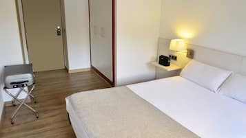 Ein Hotelzimmer mit einem Bett, einem Nachttisch mit Lampe, einem Koffer und einem Kleiderschrank.