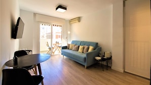 A living room with a blue sofa, a round dining table, and a TV mounted on the wall.