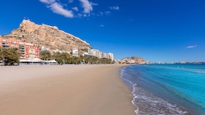 A beach with a mountain in the background, clear blue sky, and a calm sea.