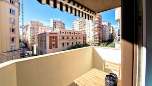 A balcony with a view of a cityscape, a table with a chair, and a potted plant.