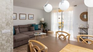 A modern living room with a sofa, dining table, and chairs. There are framed pictures on the wall, a lamp, and a window with curtains. - HomeForGuest Ático Cecilia con terraza y vistas al mar en Los Cristianos (Los Cristianos)