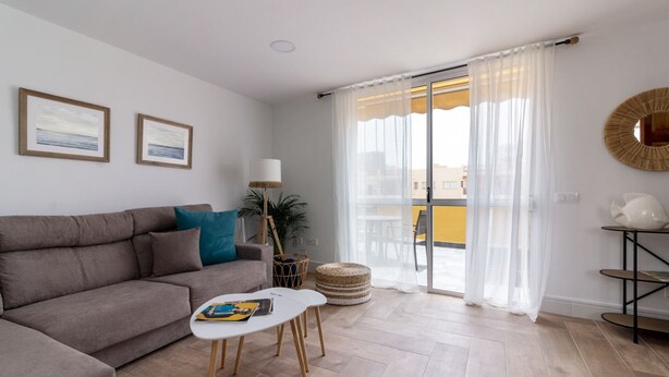 A living room with a sofa, a coffee table, a lamp, and a view of the outside through a glass door. - HomeForGuest Ático Cecilia con terraza y vistas al mar en Los Cristianos (Los Cristianos)