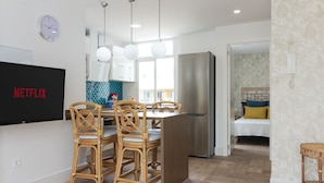 A modern kitchen with a dining area, a large refrigerator, and a flat-screen TV mounted on the wall. - HomeForGuest Ático Cecilia con terraza y vistas al mar en Los Cristianos (Los Cristianos)