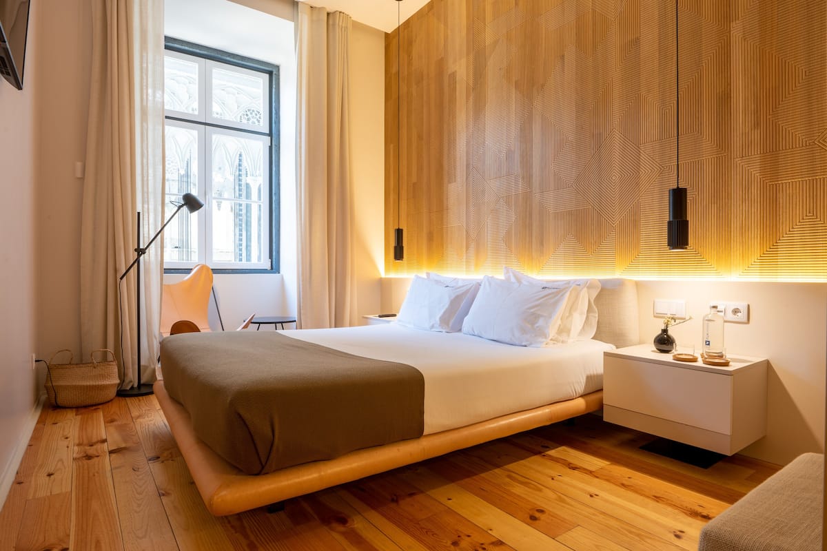 Een moderne hotelkamer met een groot bed, nachtkastjes, een lamp en uitzicht op de stad door een raam.