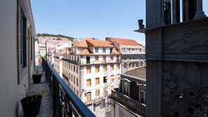 Een balkon met bloempotten, met uitzicht op een stadsgezicht met historische gebouwen en een brug.