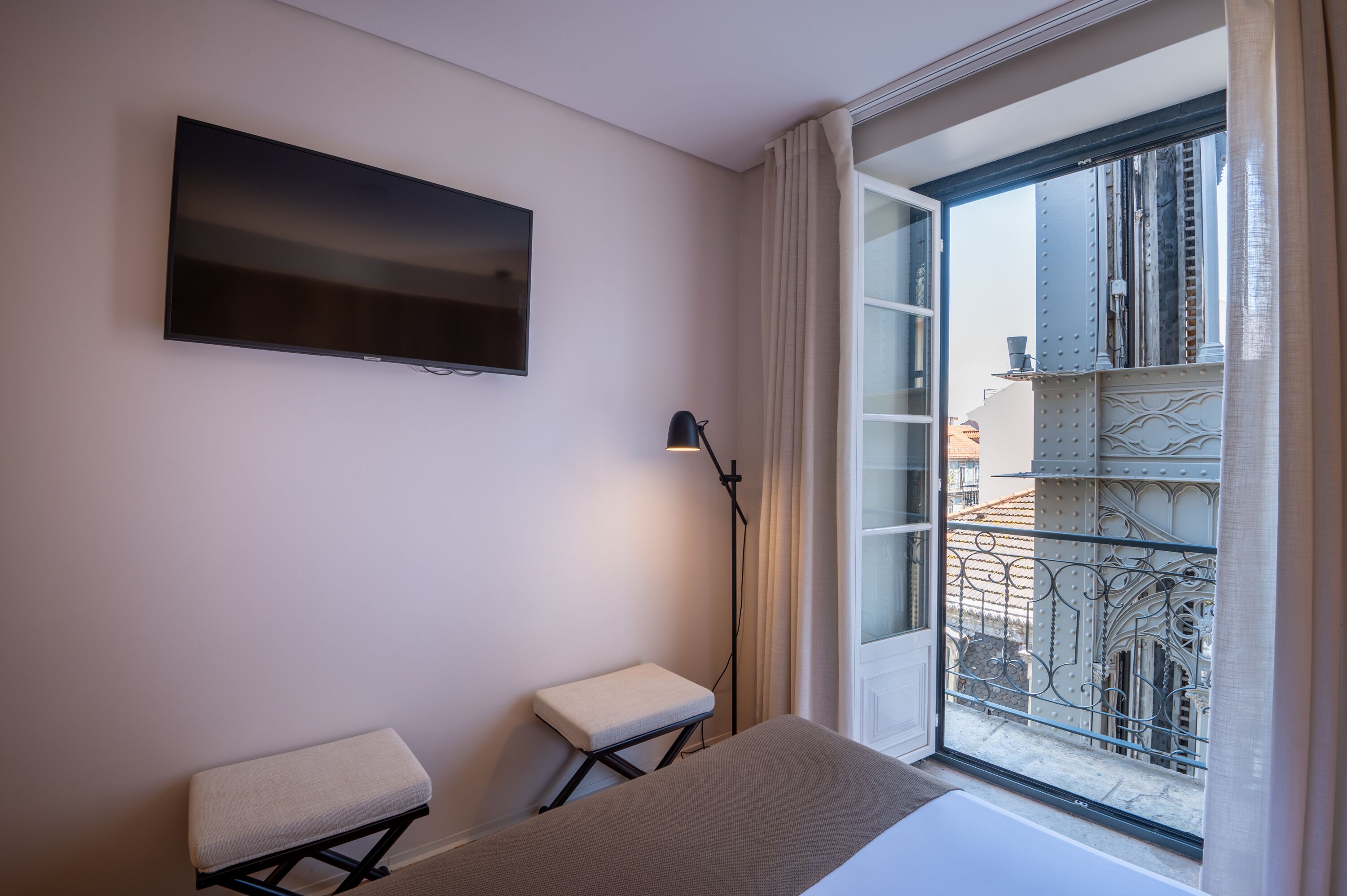 Ein modernes Zimmer mit einem Flachbildfernseher, einem Nachttisch, einer Lampe und einem Fenster mit Balkonblick.