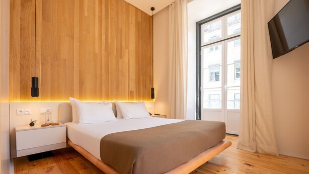 Een moderne slaapkamer met een houten hoofdeinde, een groot bed, een nachtkastje, een flatscreen-tv en een raam met gordijnen.