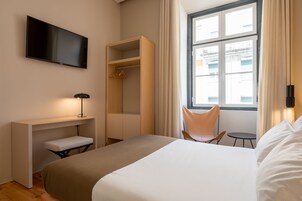 Ein Hotelzimmer mit Bett, Schreibtisch, Stuhl, Fernseher und einem Fenster mit Vorhängen.