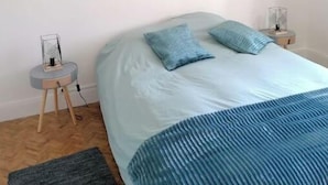 A bedroom with a bed, two pillows, a macrame wall hanging, a small side table, and a floor lamp. - Maison Héouguère 29km from Dax and 15km from Orthez, and 5min from Amou (Castel-Sarrazin)