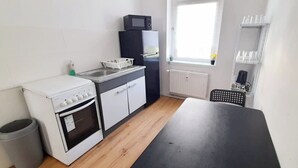 Une cuisine compacte équipée d’une cuisinière, d’un four à micro-ondes et d’un réfrigérateur. Une fenêtre laisse entrer la lumière naturelle et une petite poubelle est à disposition.