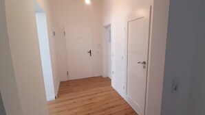 Un couloir étroit, doté d’un plancher en bois et de murs blancs, qui mène à une porte munie d’une poignée.