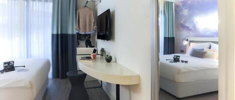 A hotel room with two beds, a desk with a chair, a TV mounted on the wall, and a window with curtains.