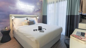 Ein Hotelzimmer mit einem Bett, einem Nachttisch mit einer Uhr, einer Lampe und einer Wand mit einem motivierenden Zitat.