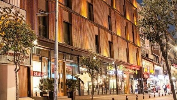 Ein mehrstöckiges Hotel mit moderner Fassade, großen Fenstern und Blick auf eine Straße mit Geschäften.