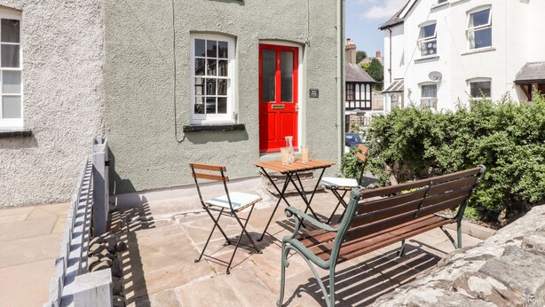 A building with a red door, a window, and a bench. - Kooky Cottage (Brecon)