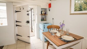 A dining area with a wooden table set for two, a blue refrigerator, and a red hanging light fixture. - Kooky Cottage (Brecon)