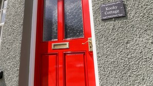 A red door with a glass panel and a metal handle, a number '1' above the door, and a sign reading "Kooky Cottage". - Kooky Cottage (Brecon)