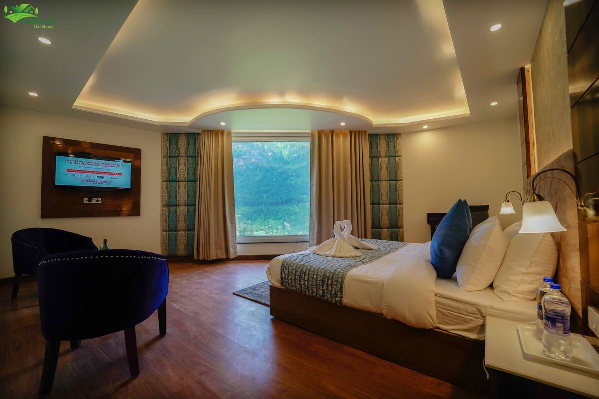 A hotel room with a bed, a TV mounted on the wall, a chair, and a window with curtains.