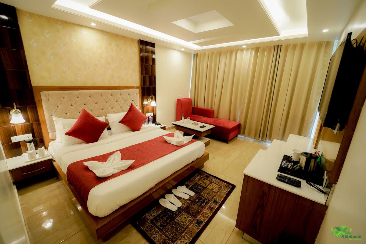 A hotel room with a large bed, a red chair, a small table, and a desk with a remote control.