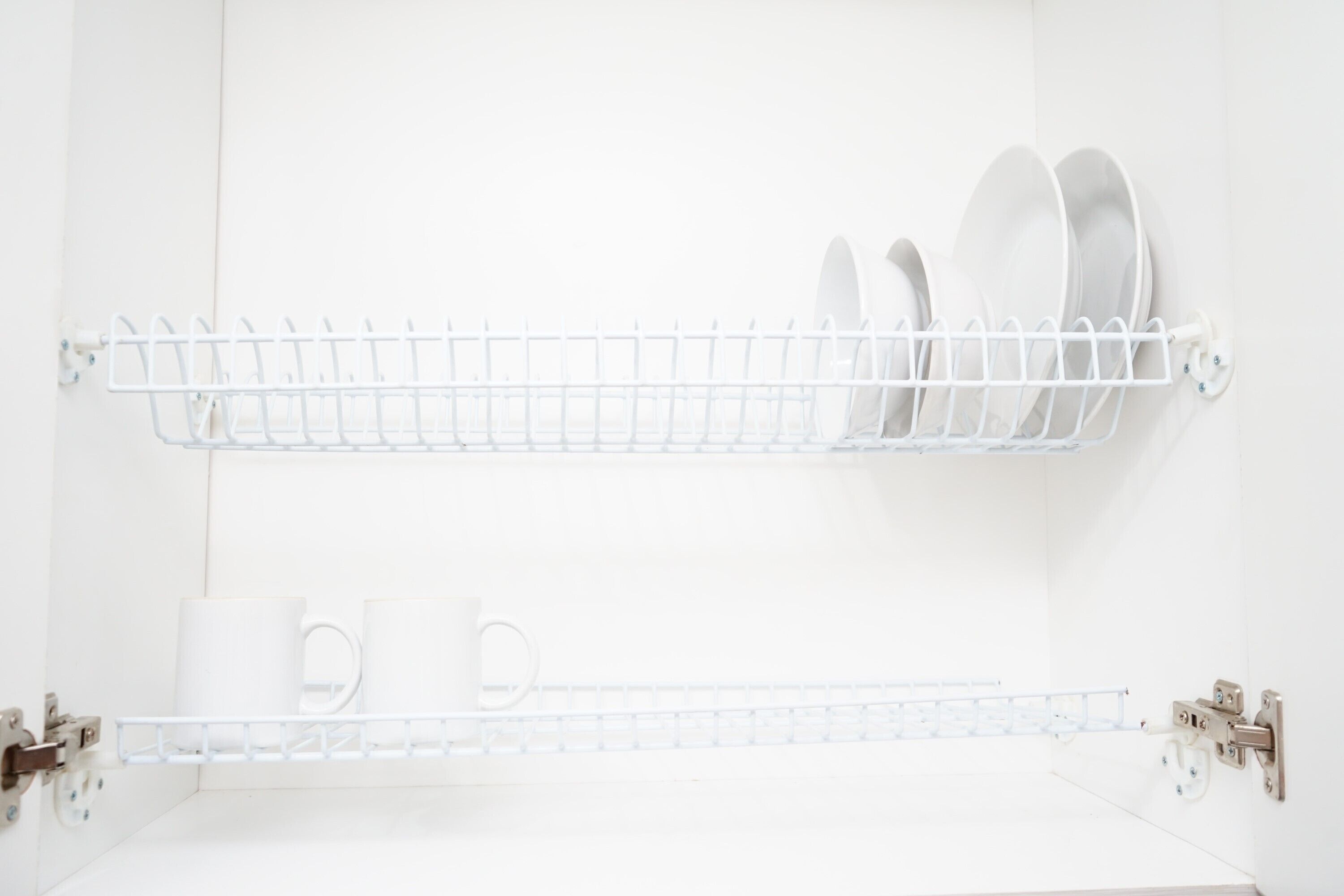 Un baño blanco con dos estantes blancos montados en la pared, cada uno con vajilla blanca y una taza blanca.