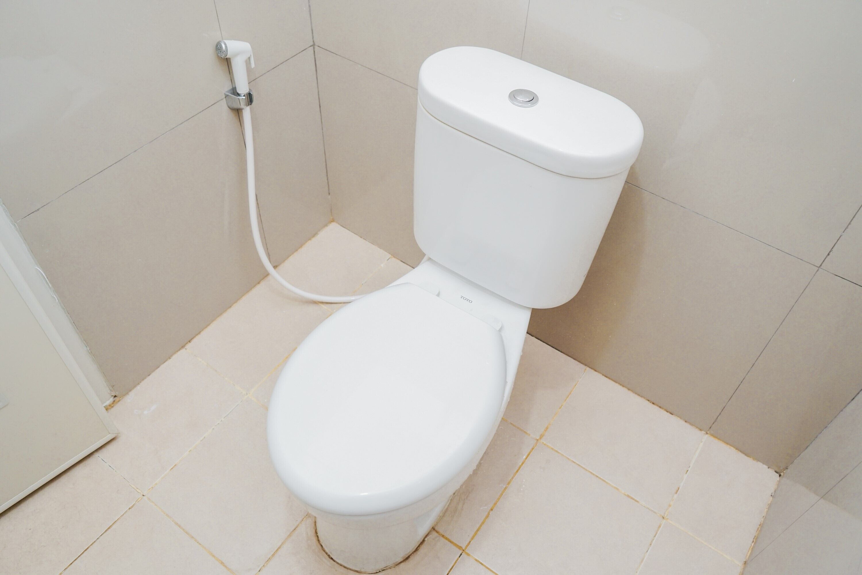 A white toilet with a bidet attachment in a bathroom with tiled flooring.