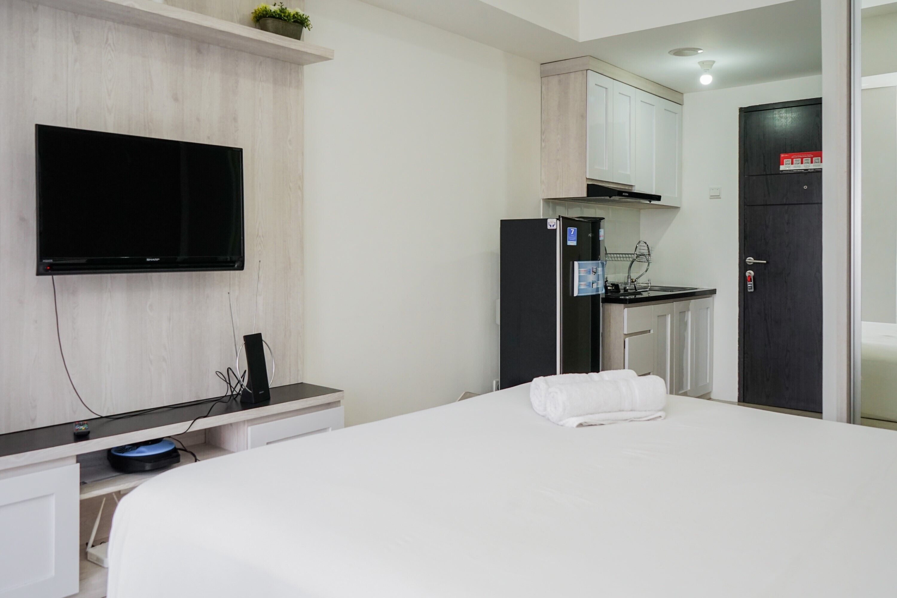 A hotel room with a bed, a TV mounted on the wall, a small kitchenette, and a door with a sign.