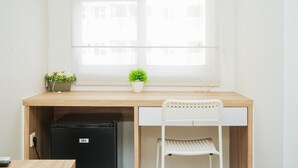 Un espacio de trabajo compacto con un escritorio de madera, una silla blanca, un refrigerador negro pequeño y dos macetas en el alféizar.