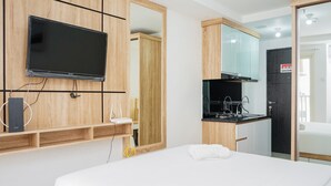 Una habitación de hotel moderna con una cama grande, un televisor de pantalla plana montado sobre un panel de madera, una pequeña kitchenette y un mueble espejo.