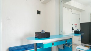 Ein sauberes, modernes Zimmer mit blau-weißer Farbgestaltung, einem Flachbildfernseher, einer kleinen schwarzen Box auf der Ablage und einem Spiegel, der den Raum widerspiegelt.