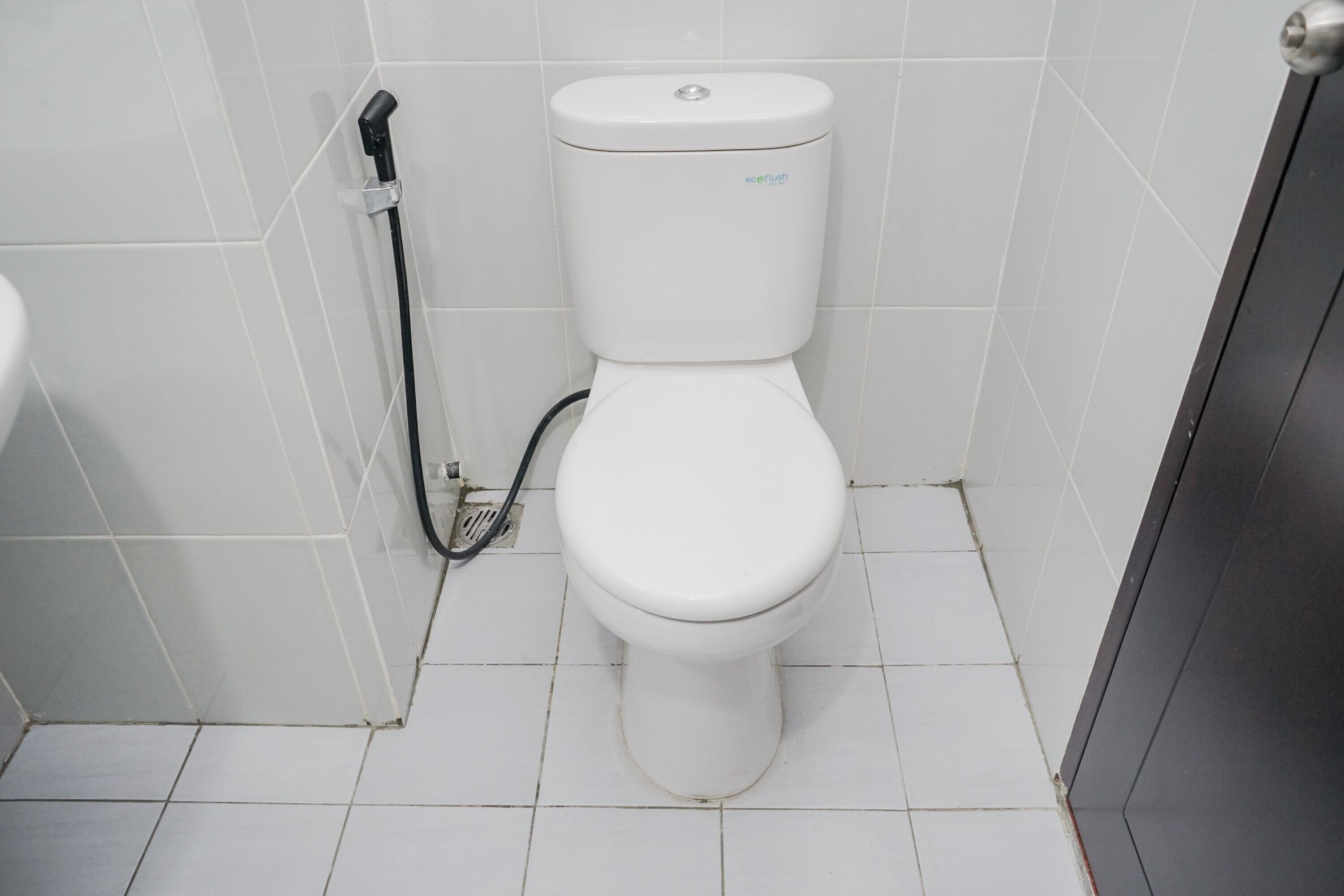 Des toilettes blanches avec un tuyau noir, une étiquette de marque bien visible et un sol carrelé.