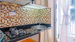A kitchen with a tiled backsplash, a stainless steel sink, and a gas stove. - Cozy Stay 2BR Bassura City Apartment (Jakarta)