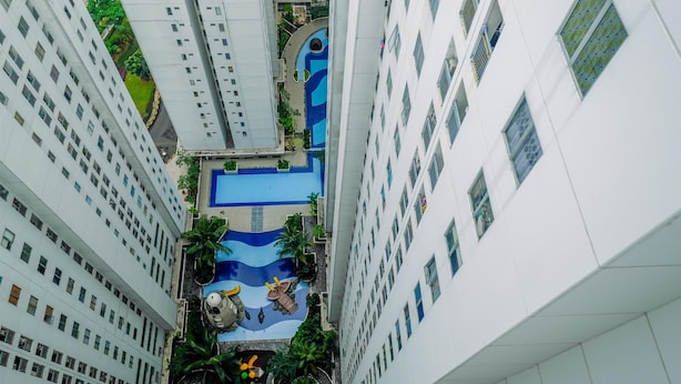 A high-rise building with a rooftop pool featuring a blue wave design, surrounded by greenery and palm trees. - Cozy Stay 2BR Bassura City Apartment (Jakarta)
