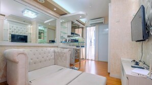 A modern hotel room with a white sofa, a television mounted on the wall, and a kitchen area visible through an open door. - Cozy Stay 2BR Bassura City Apartment (Jakarta)
