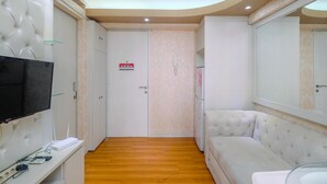 A hotel room with a TV, a desk with a computer, a sofa, and a mirrored wardrobe. - Cozy Stay 2BR Bassura City Apartment (Jakarta)