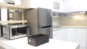 A modern kitchen with stainless steel appliances, including a microwave and refrigerator, and a countertop with a black box labeled "Travelio." - Best Location 2BR Tamansari La Grande Apartment (Bandung)